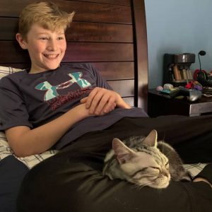 Smiling child with American Shorthair cat sleeping on lap
